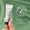 En hand håller en liten vit tub med Rejuvenating Eye Cream 10ml mot en salviagrön bakgrund med bladskuggor.