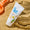 Vit tub med SPF50 solcreme på sand bredvid en orange plastspade, med det nedre vänstra hörnet bortklippt.