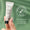 En hand håller en tub med Green People Scent Free Eye Cream 10ml mot en grön bakgrund med en Dermatologically Tested-ikon.