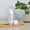 A white bottle of Scent Free Ultra Calm Serum rests on a small bamboo tray next to a tropical green palm leaf.