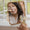 En hand håller en flaska Age Defy+ Collagen Boost Face Oil Elixir medan en kvinna applicerar produkten i en spegelbild.