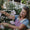 A smiling mature woman gardens outdoors near pink flowers, highlighting benefits of Age Defy+ Collagen Boost Vitamin C Serum.