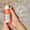Händer som håller en orange och vit flaska med Oy Clear Skin Cleansing Moisturiser med märket Dermatologically Tested.